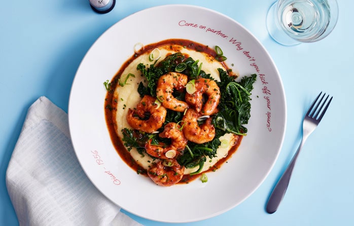 Plate of prawns on top of mash and greens