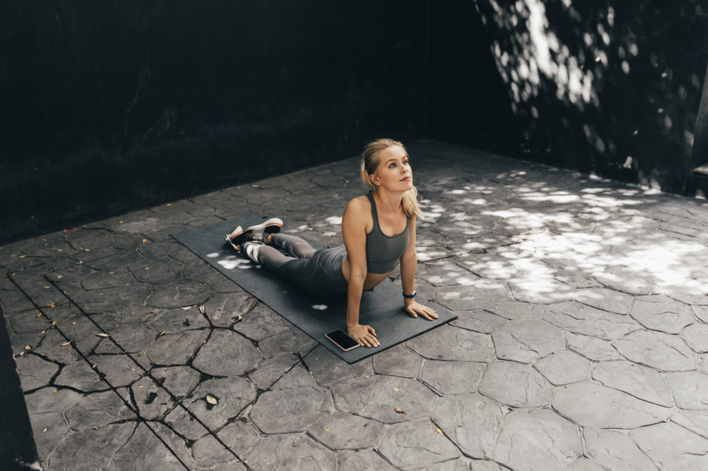 An attractive young woman doing exercises on a yoga mat by following an online app on her smartphone.